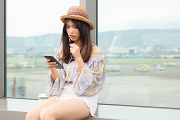 Beautiful young woman in earphones sitting outdoors, talking on mobile phone, drinking coffee.