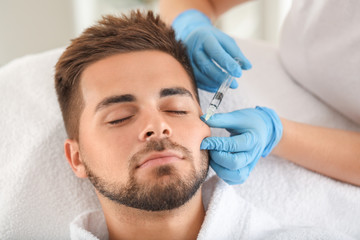 Obraz na płótnie Canvas Handsome man receiving filler injection in beauty salon