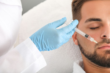 Handsome man receiving filler injection in beauty salon