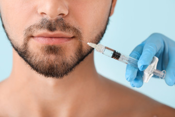 Handsome man receiving filler injection on color background, closeup