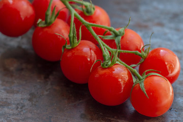 Fresh organic bright small red cherry tomatoes with green branch on dark brown and black rustic metal background