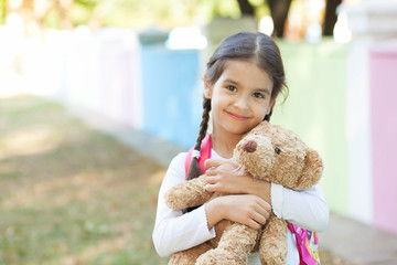 Adorable little child girl with a teddy bear outdoors. School time. 