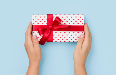 Female hands holding a lovely gift box on blue background