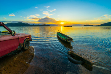 Old pickup truck parked on the waterfront with sunset at Bang phra reservoir ,sriracha chon buri,  thailand - obrazy, fototapety, plakaty