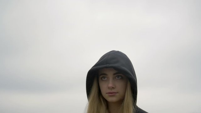 Slow motion - Young blonde girl looking at camera with hood up staring with eyes