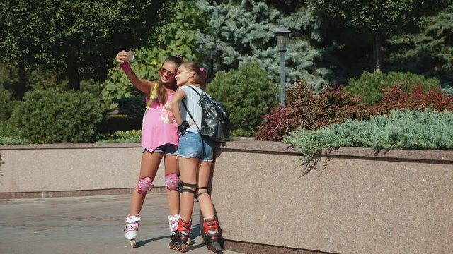Girls rollerblading take a selfie on a smartphone. Best girlfriends teenagers being photographed in a summer park. The concept of true friendship