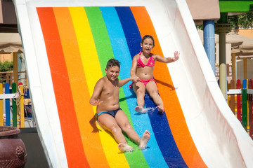 Summer bright sunny at the water park brother and sister with slide down the hill/