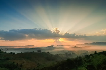 Mountain view misty morning of top hills around with sea of fog in valley and sun-rays in cloudy sky background, sunrise at Wat Kong Niam View Point, Khao Kho, Thailand.
