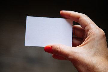 Female hand with red nails is holding a blank business card. Soft focus.