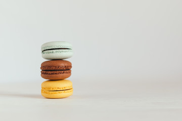Three French macarons on a white wooden table. Multicolored macarons. White background.