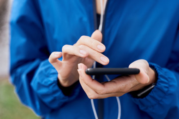 Female hands holding smart phone with earphones against blue raincoat