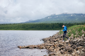 Man in blue rain coat jogging at rocky river bank
