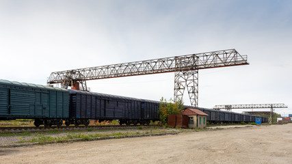 Large metal gantry cranes at a on the railway platform, standing on freight wagons for storing goods. Type of bearing metal structures of gantry crane against the blue sky