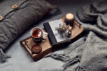 Fototapeta na wymiar Cozy home with cup of tea with steam, blanket, book and candles. Hygge home interior