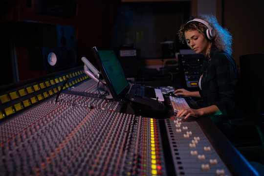 Female music producer working at the mixing desk in a sound studio