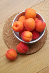 Fresh ripe apricots in a white bowl on wooden table. Prunus armeniaca fruits