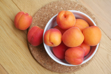 Fresh ripe apricots in a white bowl on wooden table. Prunus armeniaca fruits