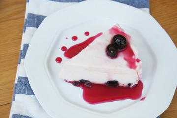 Cheesecake with sour cherries and sauce on a plate on wooden table. Sour cherry cheesecake on a plate