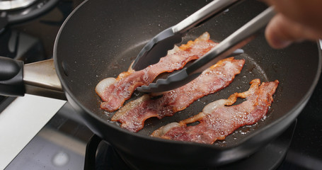 Fry bacon in pan in kitchen for breakfast