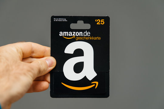 PARIS, FRANCE - APR 1, 2018: Man holding against gray background 25 Euros Amazon gift card issued by Amazon Germany, valid in Austria as well
