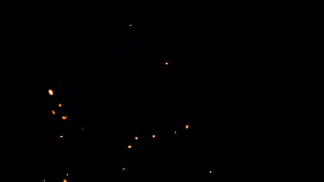 Chaotic Trajectories of Flying Sparks. Bright red-hot sparks move randomly and at different speeds on a black background. Filmed at a speed of 240fps