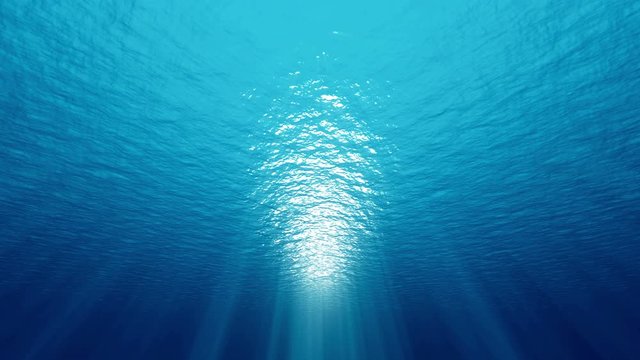 Deep underwater ocean with small waves ripple and sun light rays. 4K seamless loop