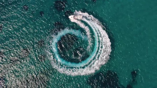 Luftaufnahme eines Motornoots welches einen Kreis f&auml;hrt und Luftblasen und Wellen im t&uuml;rkisem Ozean hinterl&auml;sst
