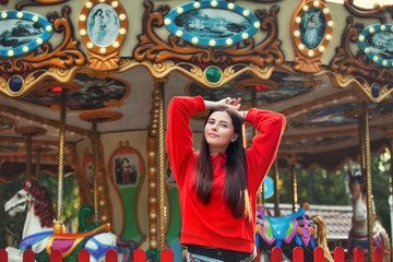 Young beautiful brunette woman happy in the Park on the background of bright colored carousel
