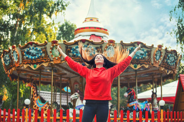 Young beautiful brunette woman happy in the Park on the background of bright colored carousel