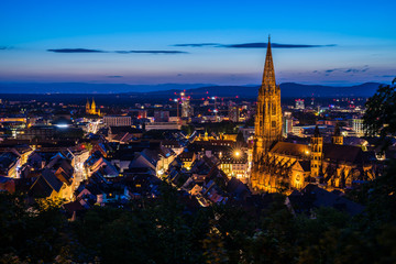 Fototapeta na wymiar Germany, Freiburg im breisgau city in black forest nature with illuminated ancient historical muenster church surrounded by houses, aerial perspective by night