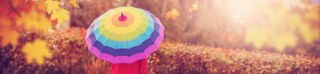 Boy holding colourful umbrella under rain in autumn