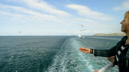 Two women feeding the seagulls by hand with bread on the deck of cruise ship. Greece. 4K