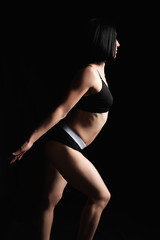 woman with a muscular body is dressed with a black topic and shorts stands sideways, the leg is set forward