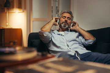 mid aged man listening music with headphones on phonograph, relaxed in sofa at his home