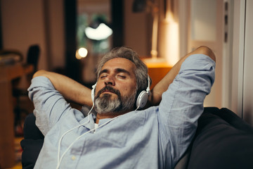 mid aged man listening music with headphones , relaxed in sofa at his home