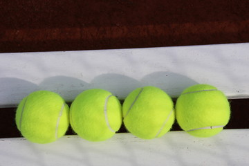 Four yellow tennisballs in summer on a white bench