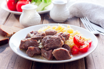 Beef stew with mashed potatoes on a white plate on a wooden table, horizontal