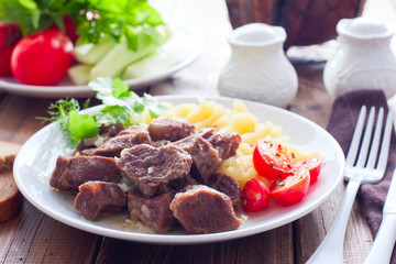 Beef stew with mashed potatoes on a white plate on a wooden table, horizontal