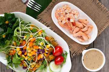 Fresh salad plate with shrimp, salmon, tomato and mixed greens  on wooden background .