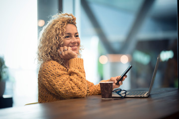 Cheerful happy people woman traveler wait at the airport gate for delay flight using modern technology device as phone and laptop computer - defocused background with bokeh