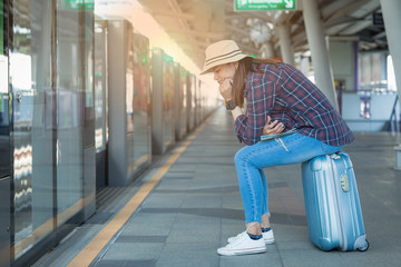 Asian woman traveler sit on the travel bag and smile while waiting train on the station, Girl happy in the plan holiday in Bangkok Thailand - travel concept image 