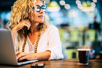 Beautiful adult caucasian people woman work at laptop computer with internet technology - concept of job and modern lady - phone and coffee on the table - defocused bokeh background