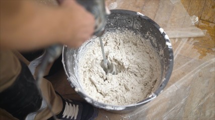 The worker mixes the mixer with plaster in a bucket with water to level the walls. mix the solution in a bucket.