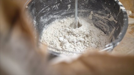 The worker mixes the mixer with plaster in a bucket with water to level the walls. mix the solution in a bucket.