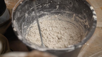 The worker mixes the mixer with plaster in a bucket with water to level the walls. mix the solution in a bucket.