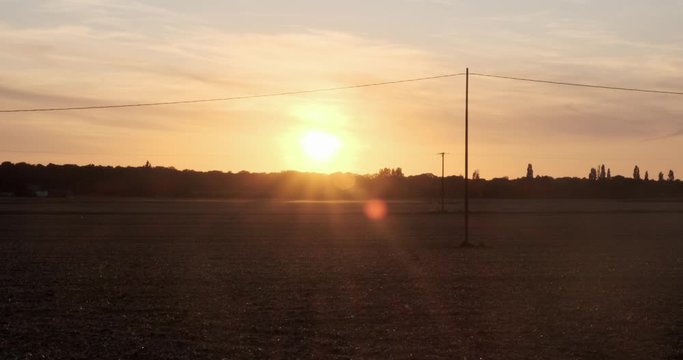 establishing shot of  fields in foreground as night falls in a backdrop of an orange sunset in normandy France