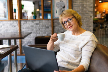 A woman sitting at a table with a Cup of tea and a laptop working in a cafe.