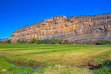 Green irrigated field with stony mountain