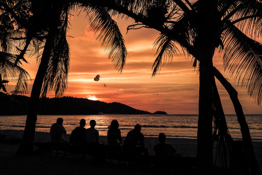 Patong beach in phuket during the sunset with six persons sit near the sea and palm trees