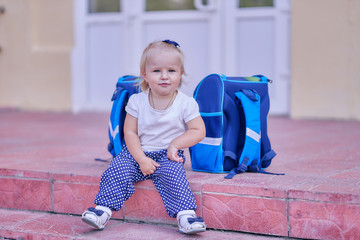 infant girl with a school bagssits at school